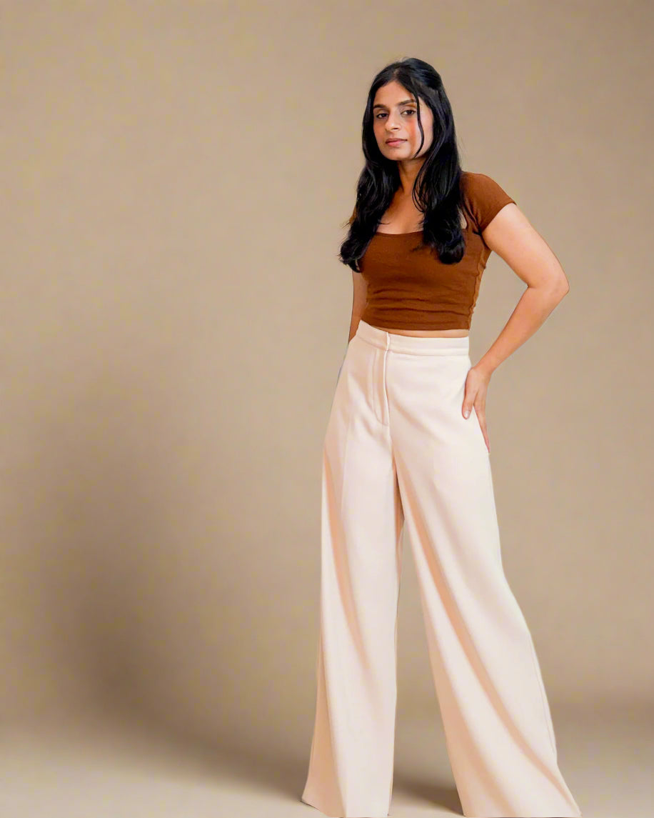 Woman wearing a brown top and beige wide-leg pants against a beige background